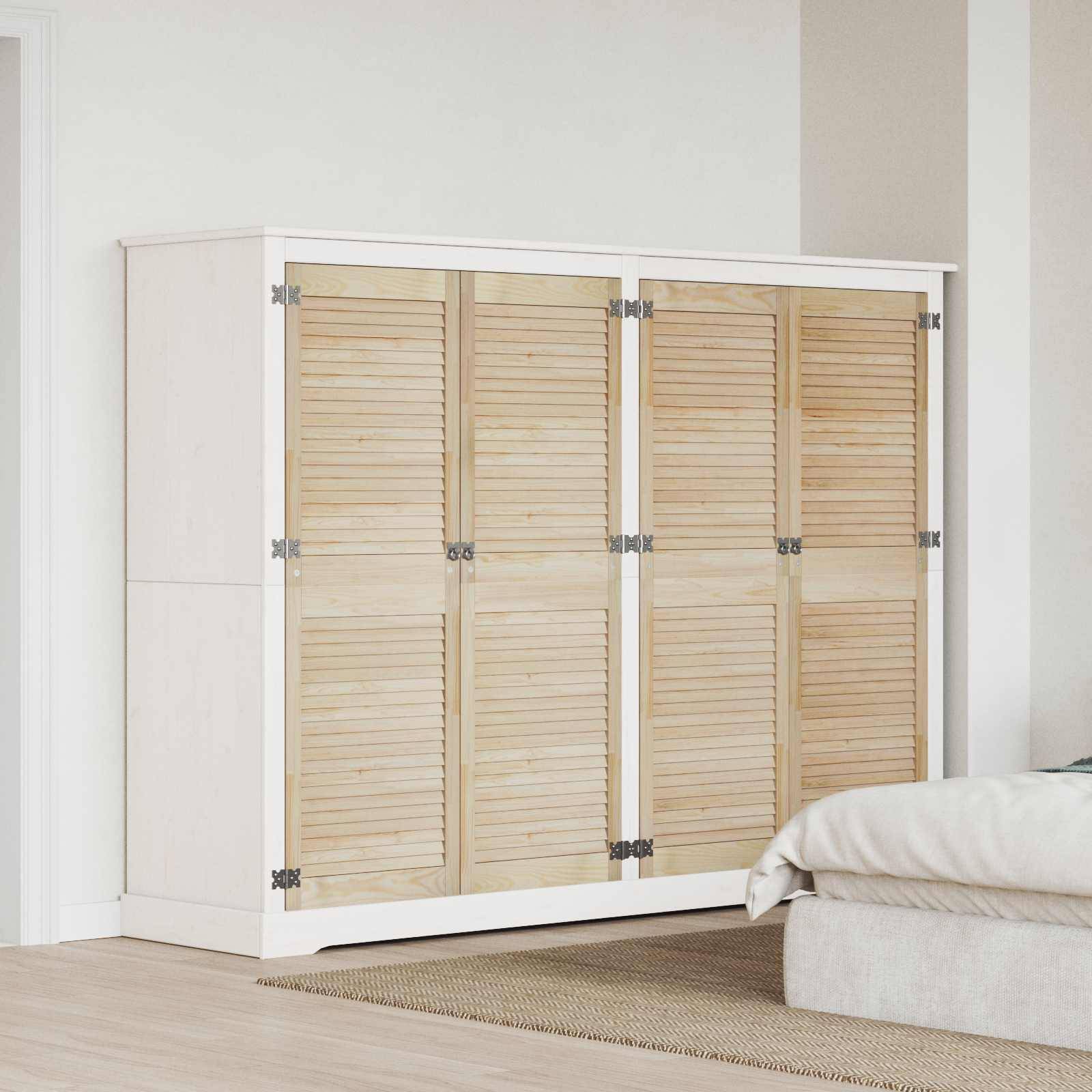 Ein großer Holzkleiderschrank mit geschlossenen Klapptüren steht neben einem Bett in einem modernen Schlafzimmer mit hellen Wänden und hellem Boden.