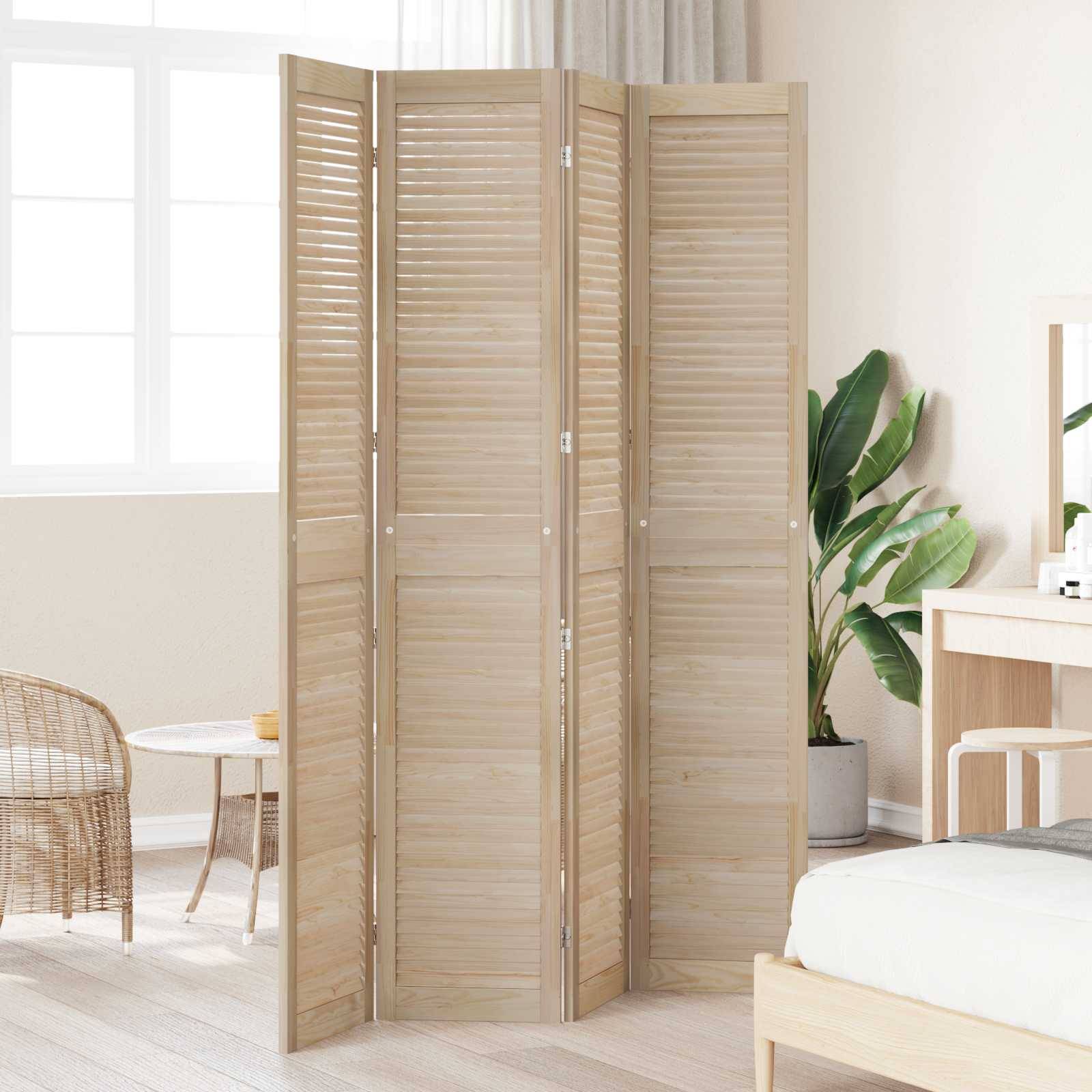 Ein hölzerner Raumteiler steht in einem hellen, minimalistischen Schlafzimmer mit Korbstühlen und einem Schreibtisch. Eine Topfpflanze bringt Grün neben dem Raumteiler.