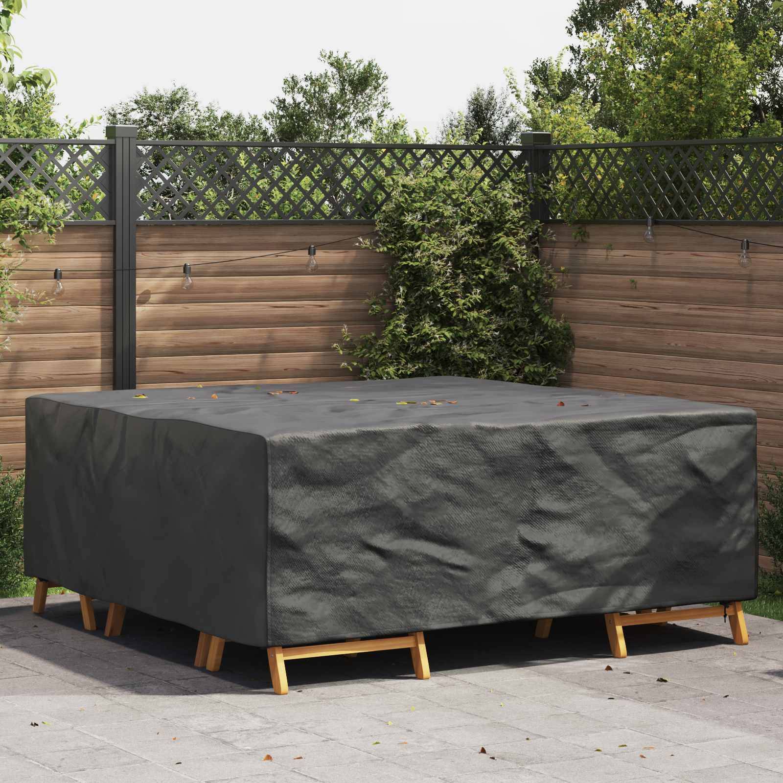 Ein großer, rechteckiger Outdoor-Tisch, der mit einer dunklen, witterungsbeständigen Abdeckung auf einer Terrasse versehen ist. Im Hintergrund ein Holzzaun und Grünpflanzen.