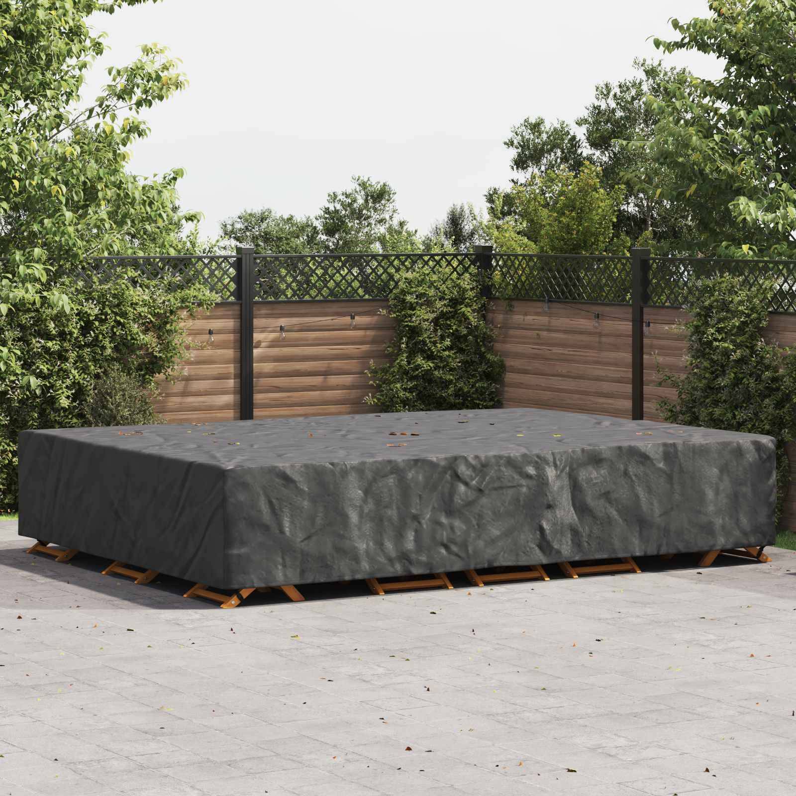 Eine schwarze Schutzabdeckung wird über eine rechteckige Outdoor-Möbelgruppe auf einer gefliesten Terrasse gelegt, umgeben von grünen Sträuchern und Holzzaun.