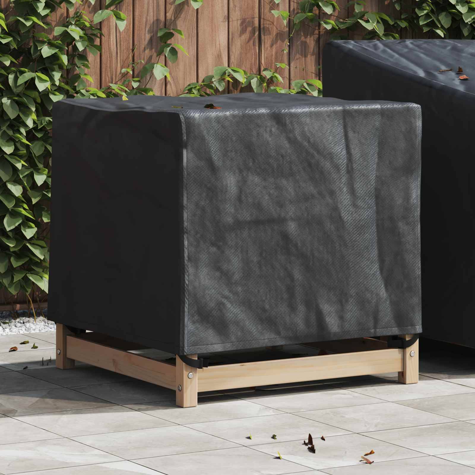 Eine schwarze Schutzabdeckung wird über eine Außenklimaanlage auf einer gefliesten Terrasse gelegt, mit einem Holzzaun und Pflanzen im Hintergrund.