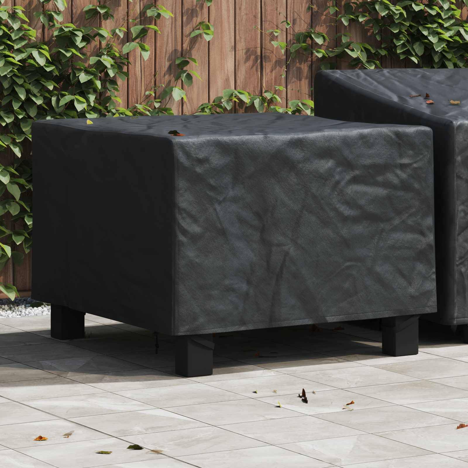 Zwei quadratische Outdoor-Hocker mit dunklen Bezügen auf einer Terrasse. Sie stehen auf hellen Bodenfliesen, mit einem Holzzaun und Grünpflanzen im Hintergrund.