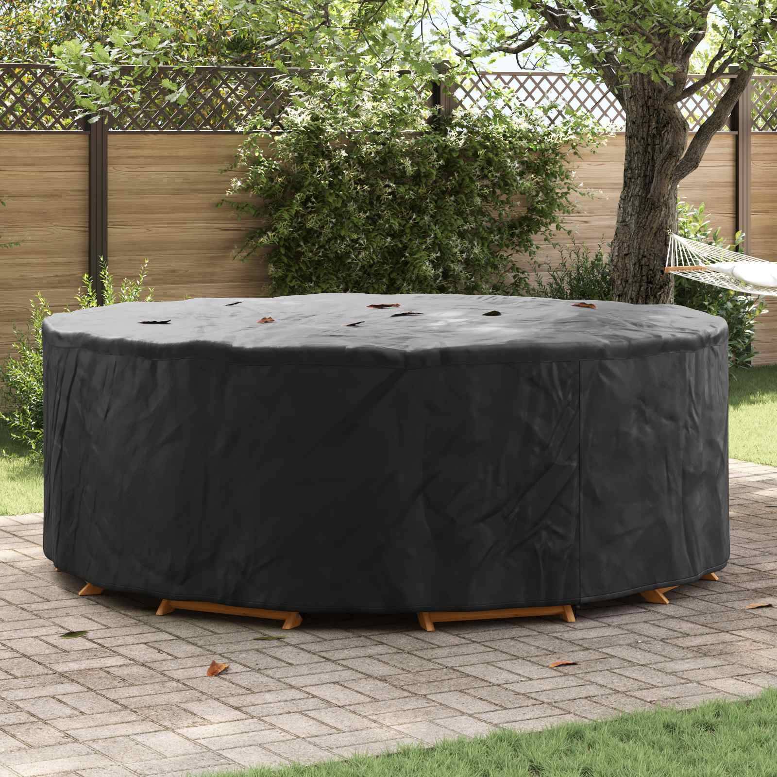 Ein rundes Outdoor-Möbelset, das mit einer schwarzen Schutzhülle bedeckt ist, auf einer Terrasse neben einem Holzzaun und Grünpflanzen.