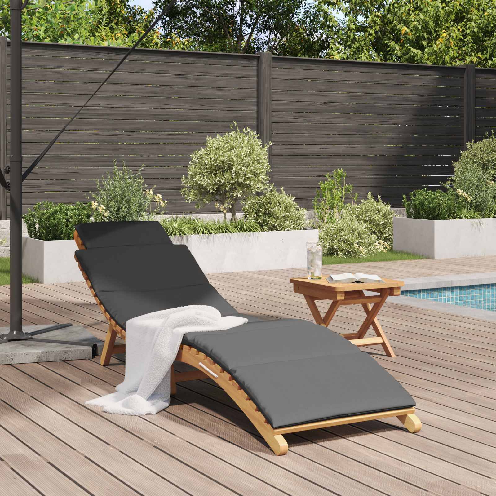 Ein Holzliegestuhl mit einem grauen Kissen und einem weißen Handtuch, das darüber drapiert ist, steht auf einem Holzdeck neben einem Pool, umgeben von Grünpflanzen.