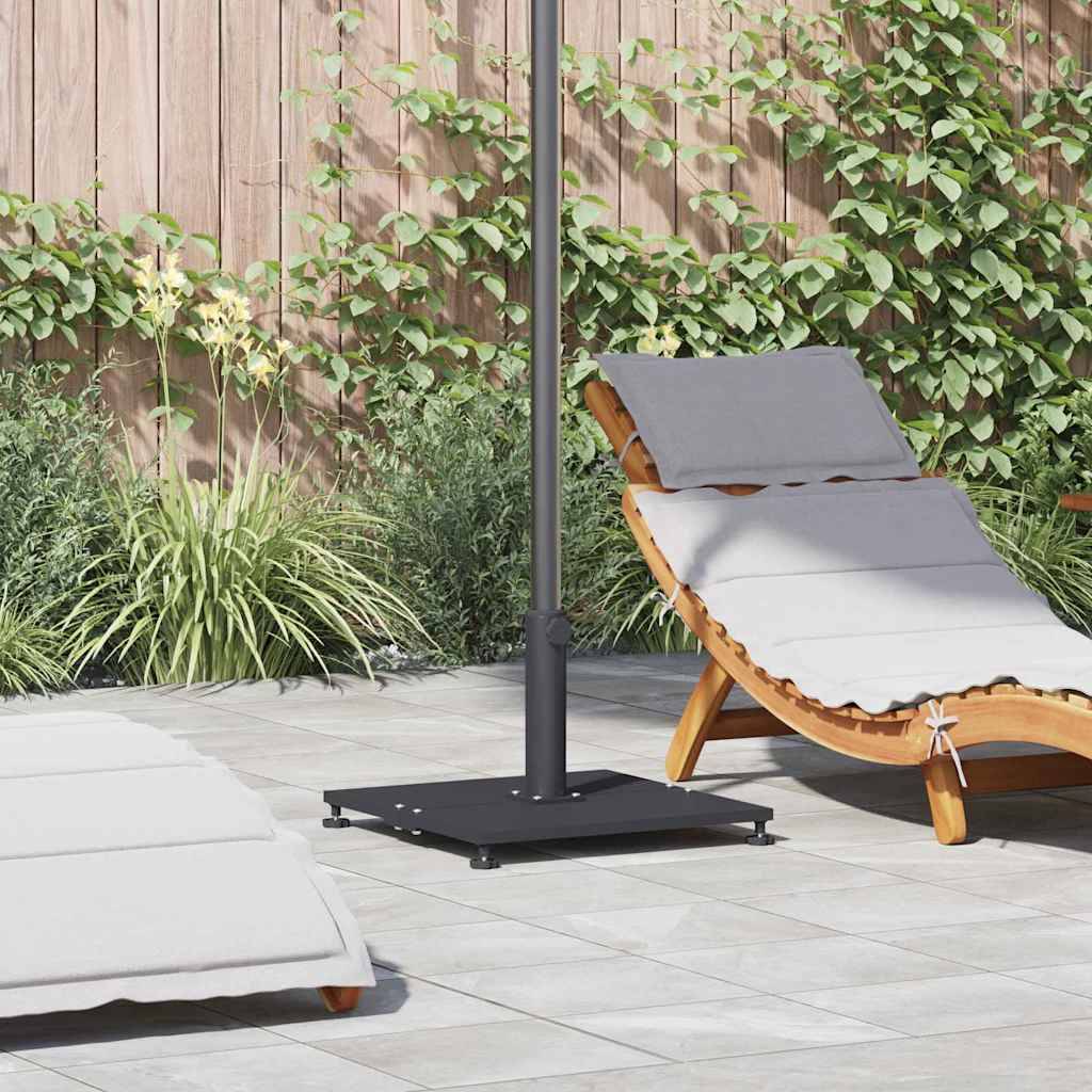 Eine Sonnenliege mit Kissen steht auf einer gefliesten Terrasse neben einer üppigen Gartenmauer. Ein großer Sonnenschirm spendet Schatten.