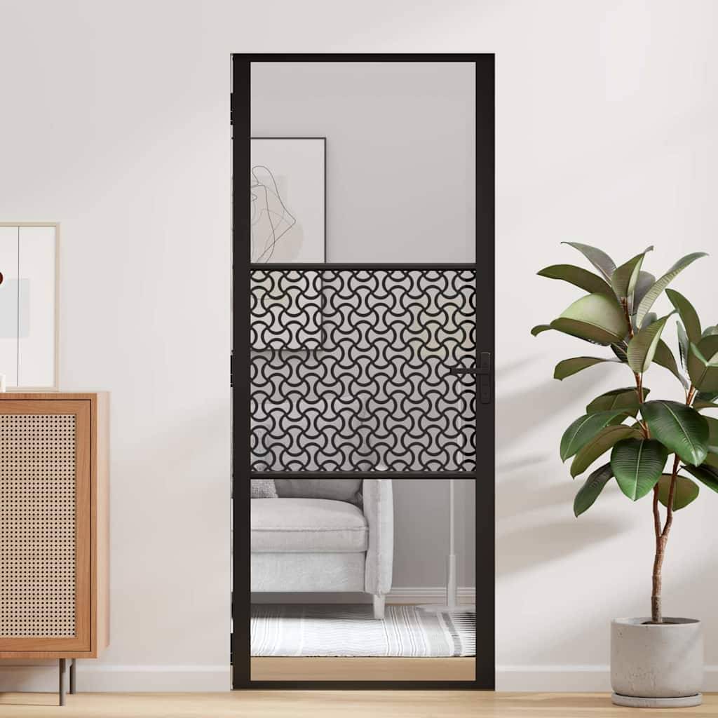 Eine moderne Innentür mit einem dekorativen schwarzen geometrischen Gitterdesign steht zwischen hellfarbenen Wänden, neben einer blattpflanze und einem beigen Sofa.
