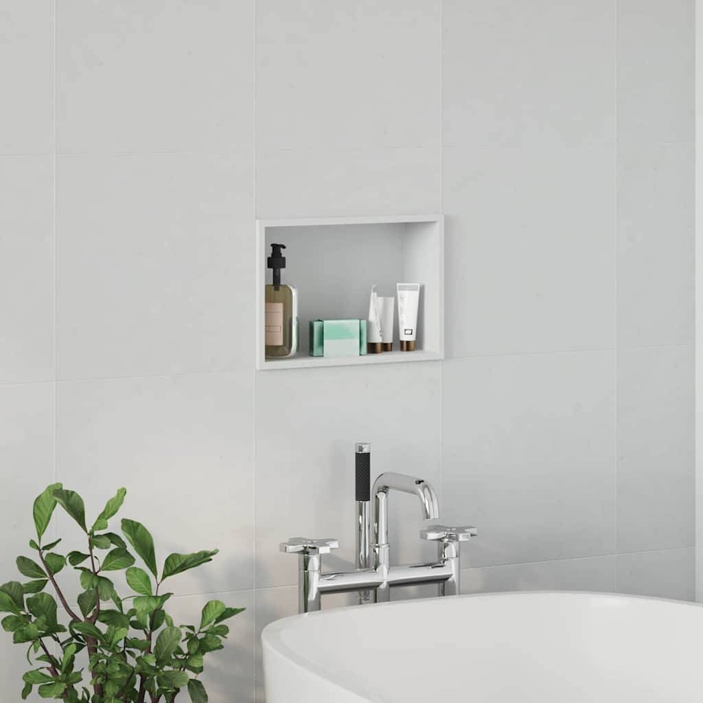 Badewannenszenerie mit einem modernen Wasserhahn, einer nahe gelegenen grünen Pflanze und einem zurückgesetzten Wandregal, das verschiedene Toilettenartikel trägt, vor einer weißen gefliesten Wand.