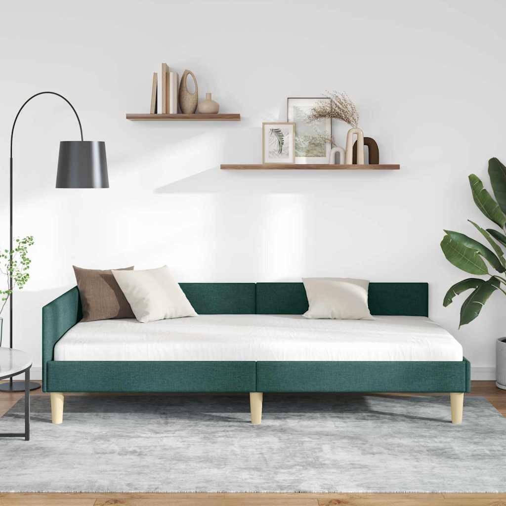Ein modernes Wohnzimmer mit einer grünen Tagesliege, zwei crèmefarbenen Kissen und einem hellgrauen Teppich. An der Wand befinden sich Regale mit Vasen und Rahmen.