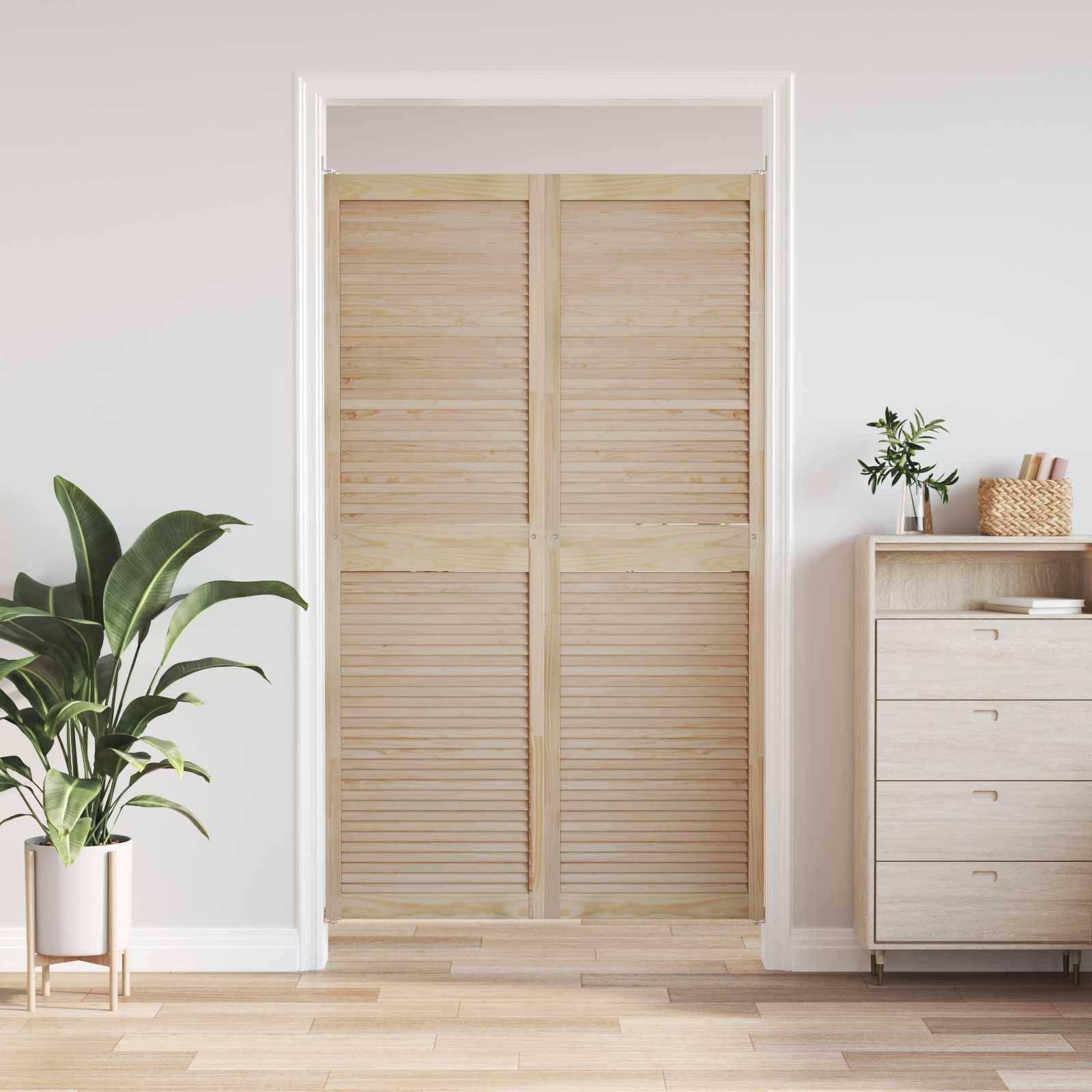 Weiße Holzjalousientür mit Rahmen, mit einer Pflanze und einer Kommode in der Nähe, die einen ruhigen, minimalistischen Innenraum schaffen.
