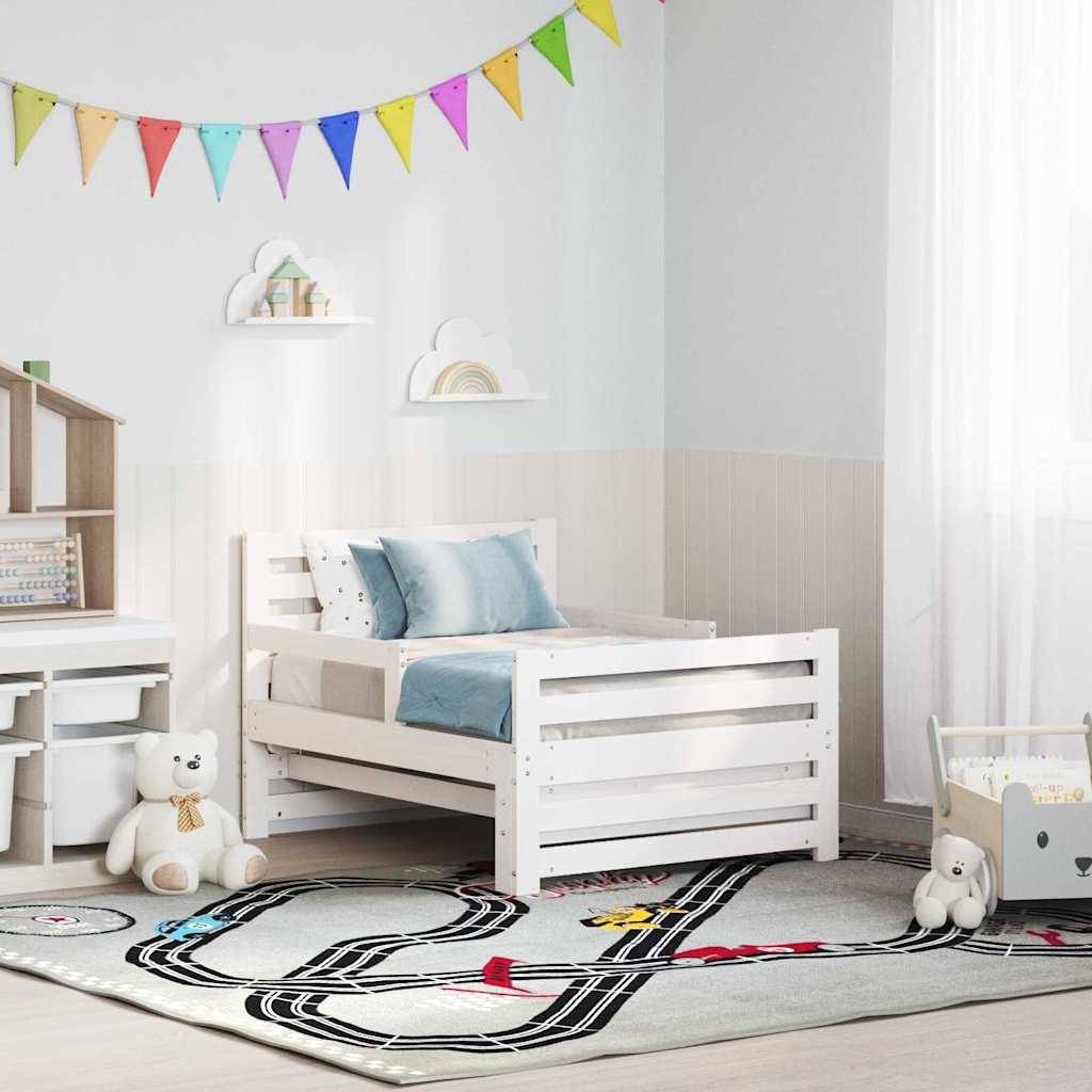Ein Kinderzimmer mit einem weißen Bett, bunter Wandgirlande und Eisenbahnmotiv-Teppich. Plüschtiere und kleine Möbel sorgen für eine gemütliche Atmosphäre.