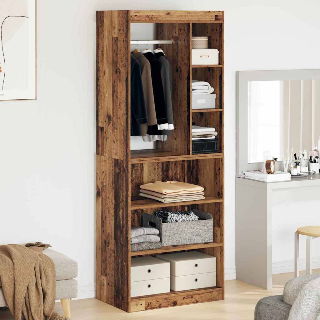 Ein Holzkleiderschrank mit offenen Regalen beherbergt Kleidung, Kisten und zusammengelegte Decken. Ein Spiegel und ein kleiner Tisch mit Toilettenartikeln stehen daneben.