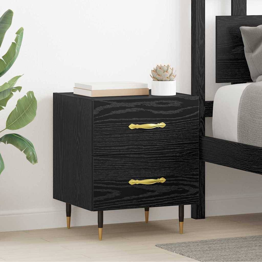 Ein schwarzer Holznachttisch mit zwei Schubladen und goldenen Griffen steht neben einem Bett. Eine kleine Pflanze und Bücher sind auf der Oberfläche platziert.