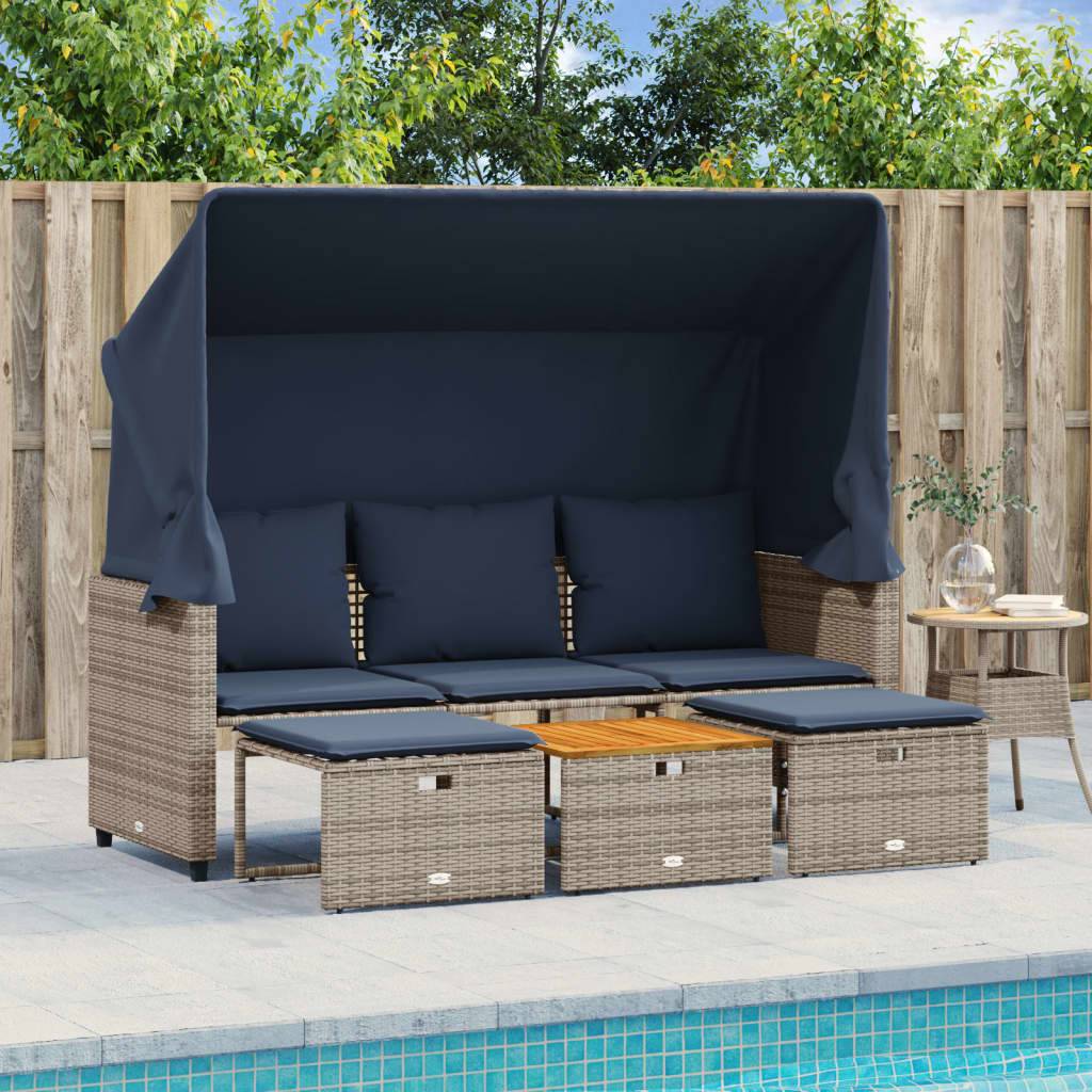 Rattan-Sonnenliege am Pool mit marineblauen Kissen und ausziehbarem Sonnendach, vier passenden Hockern und einem kleinen Beistelltisch mit einer Pflanze, in der Nähe eines Holzzauns.