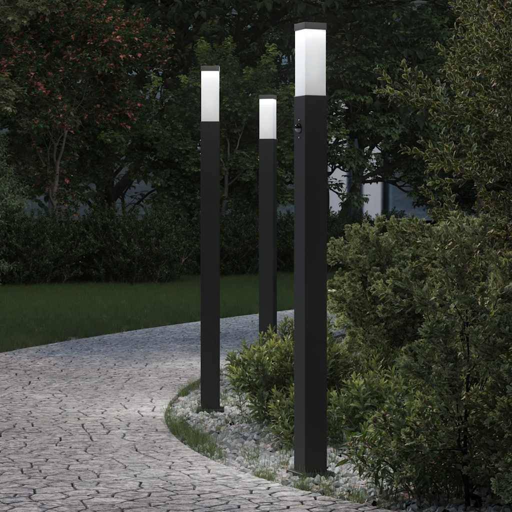Ein gewundener Steinweg, beleuchtet von modernen schwarzen Laternen, führt durch einen gestalteten Garten mit üppigem Grün in der Abenddämmerung.