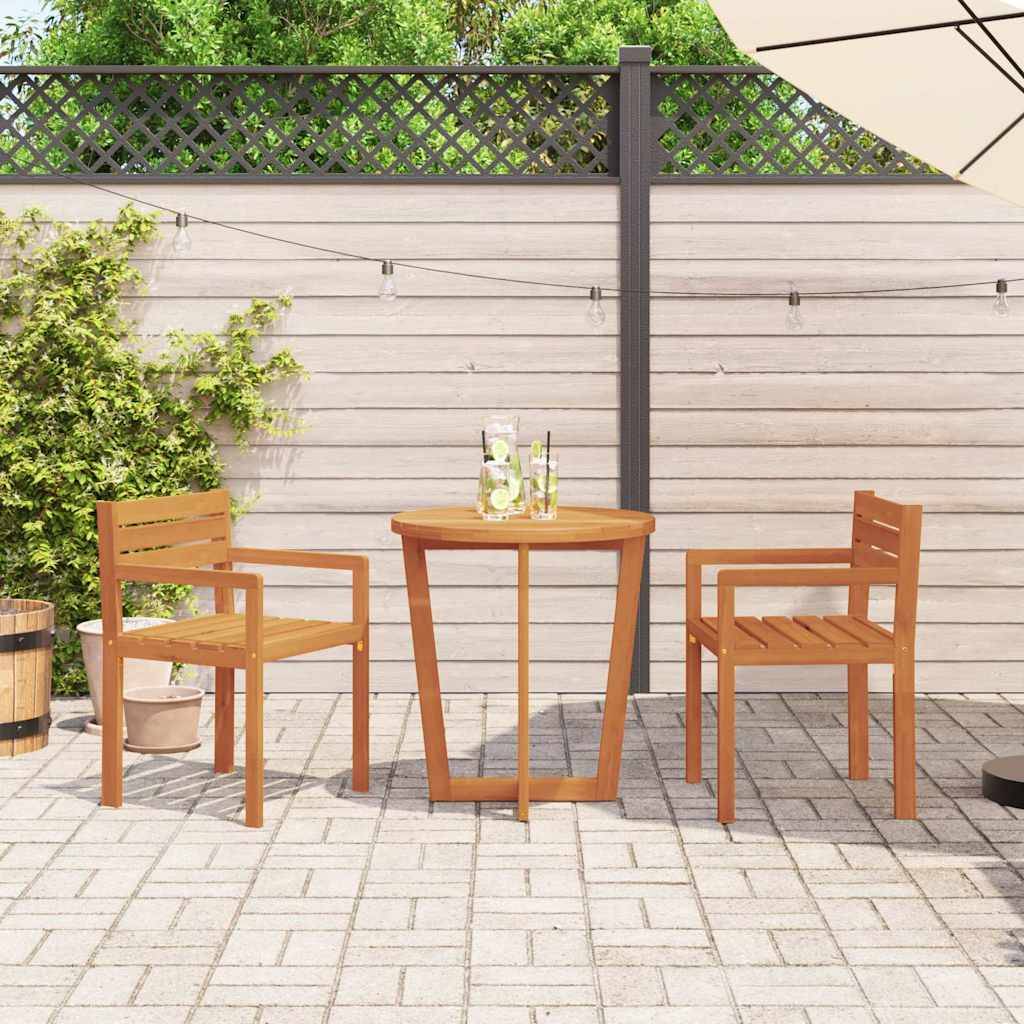 Eine Terrassenszene mit zwei Holzstühlen und einem kleinen runden Tisch auf einem Ziegelboden. Der Bereich wird von einem grünen Strauch und einem grauen Zaun begrenzt.
