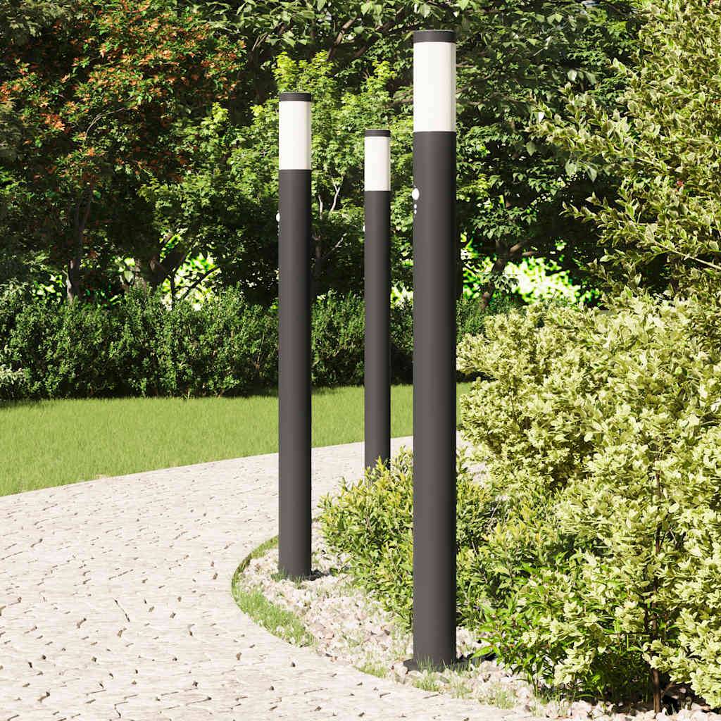 Weg mit vier hohen, schlanken Lichtmasten entlang üppiger grüner Büsche und Bäume, was eine ruhige Gartenumgebung andeutet.