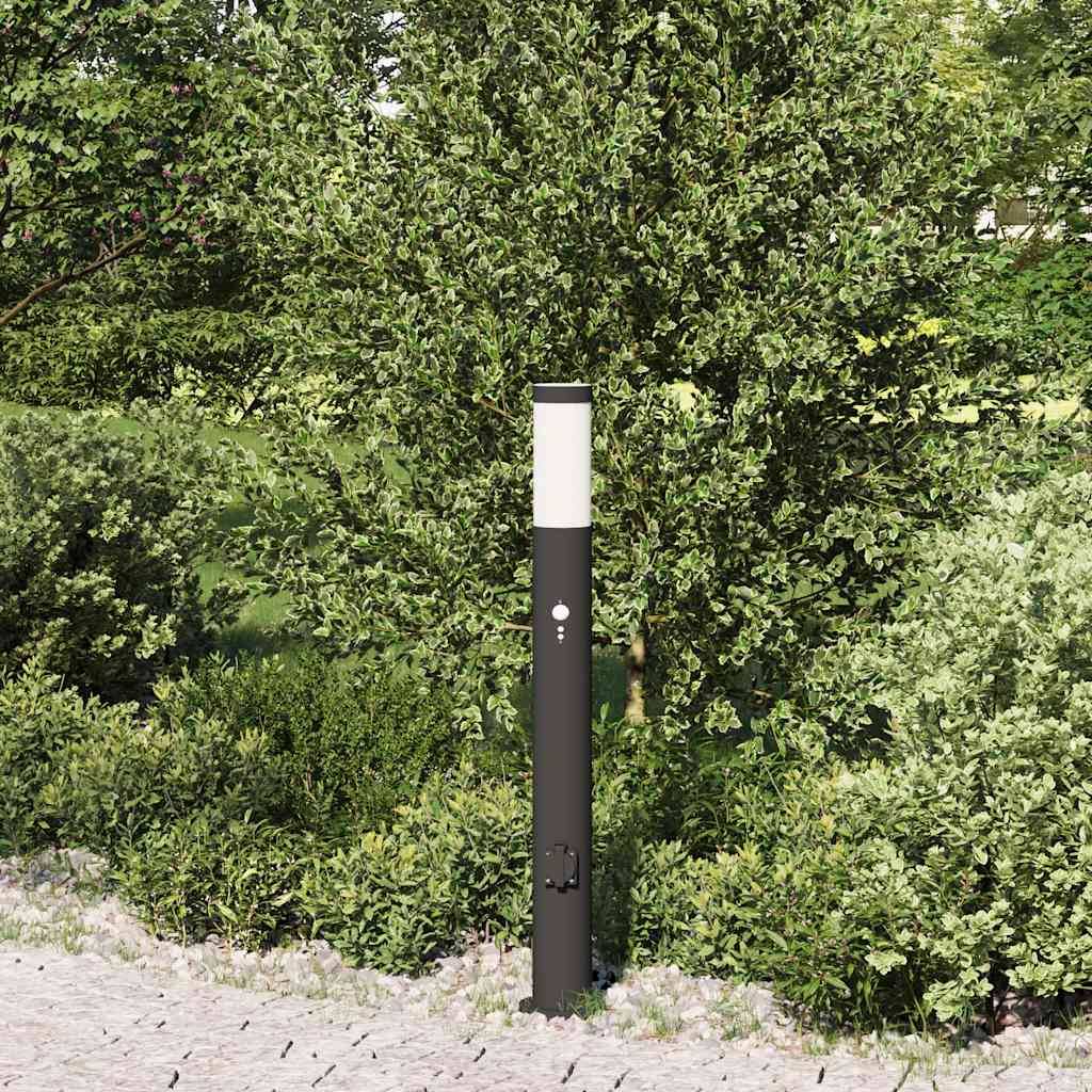 Eine schlanke schwarze Außenlampe steht in einem üppigen Garten mit grünen Sträuchern und einem Baum und verbessert die Gartenbeleuchtung.