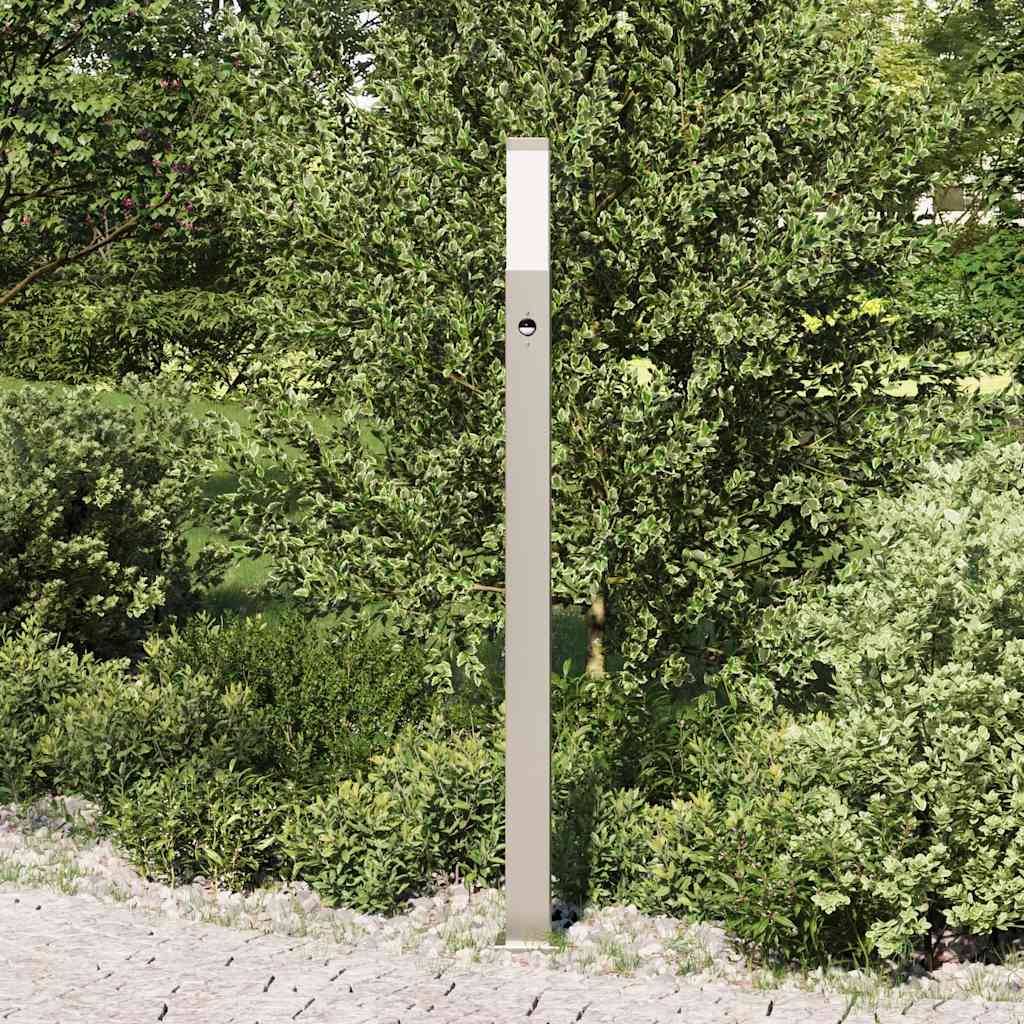Eine schlanke, vertikale Metallstange steht vor dichtem grünem Blattwerk auf einer gepflasterten Oberfläche und dient wahrscheinlich als Landschaftselement oder Lichtmast.