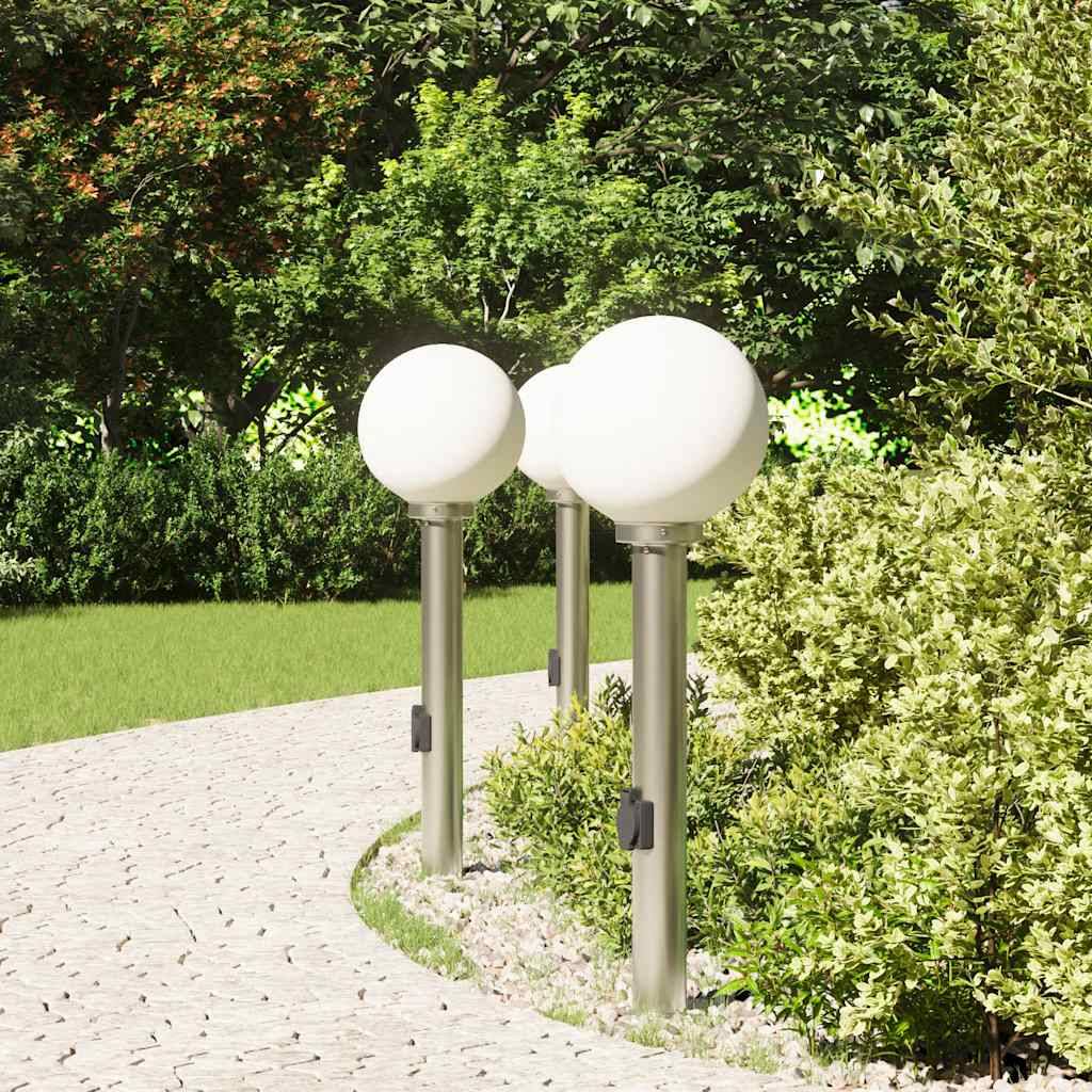 Weg, gesäumt von grünem Gras, bestückt mit modernen kugelförmigen Lampen auf Metallmasten, der in einen üppigen Garten mit dichtem Blattwerk führt.