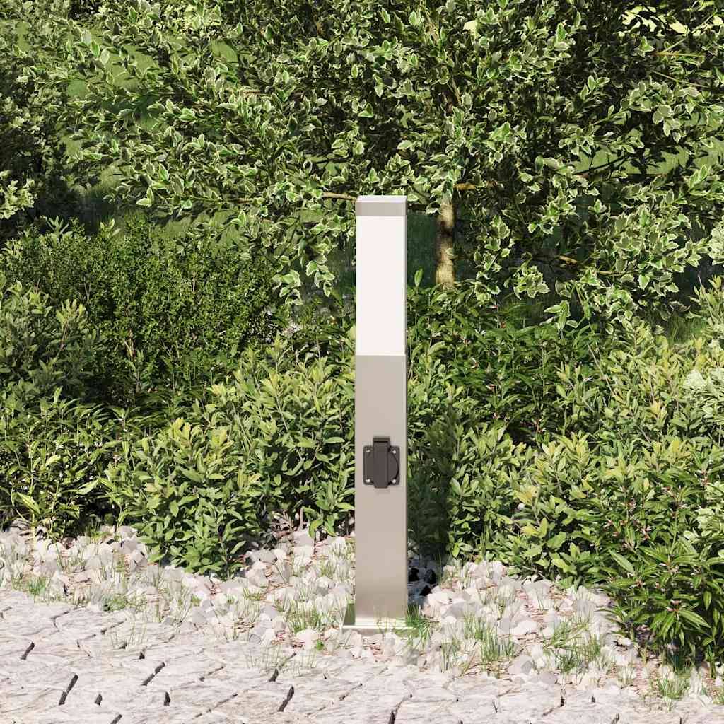 Ein rechteckiger silberner Gartenpfosten, umgeben von dichtem grünem Blattwerk an einem Steinweg, vor einer Kulisse üppiger Bäume.