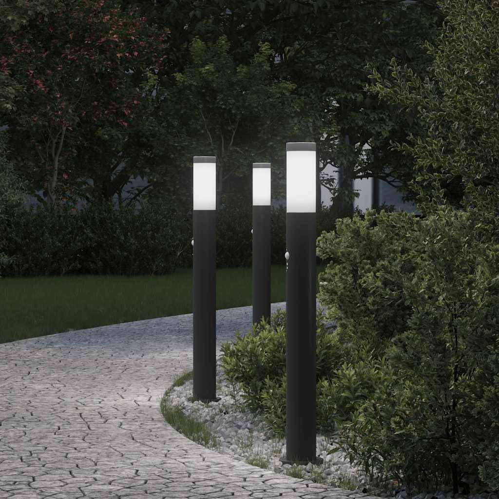 Ein gepflasterter Weg schlängelt sich durch einen Garten, beleuchtet von modernen, schwarzen Laternenpfählen. Üppiges Grün säumt den Pfad und schafft eine friedvolle Atmosphäre.