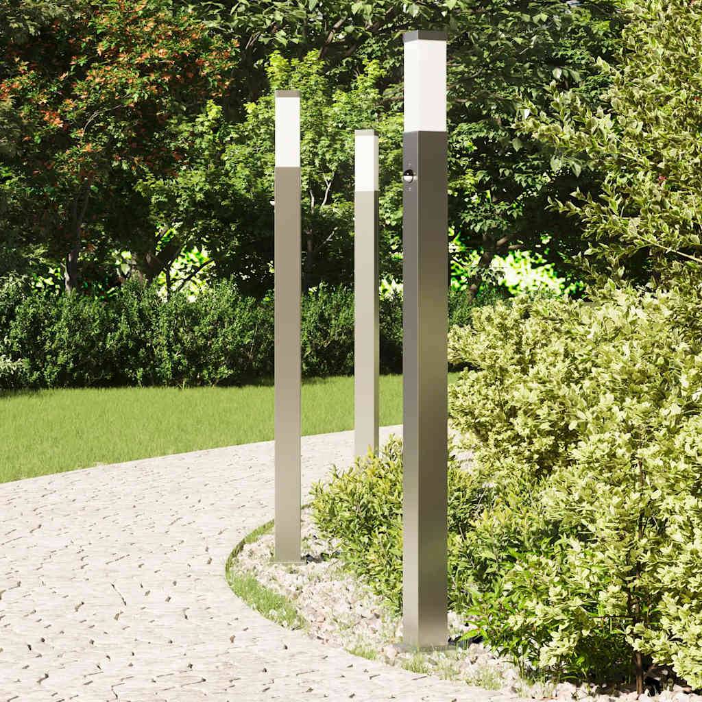 Ein Steinweg windet sich durch einen Garten, gesäumt von modernen Wegelampen und üppiger Vegetation, unter einem klaren Himmel.