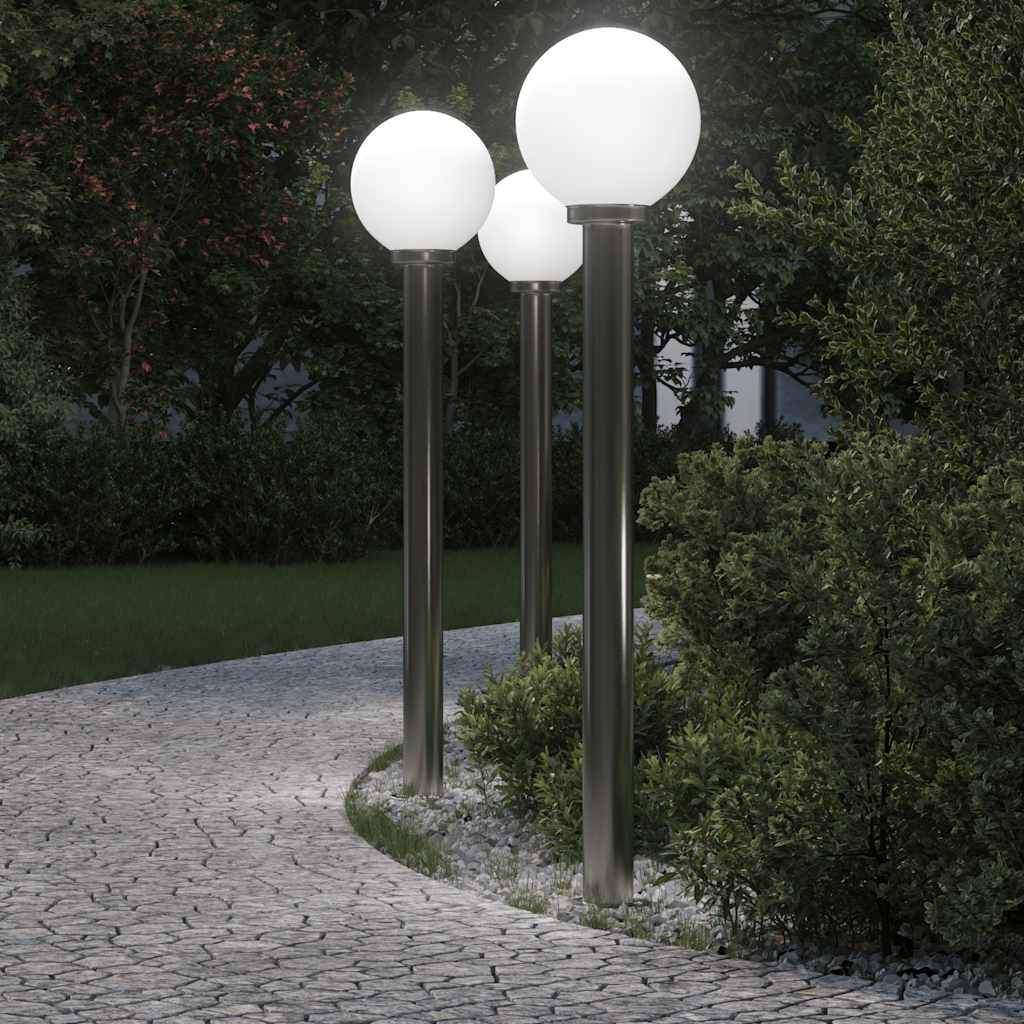 Ein geschwungener Steinweg windet sich bei Einbruch der Dämmerung durch einen Garten, gesäumt von drei kugelförmigen Straßenlampen, die die Szene beleuchten.