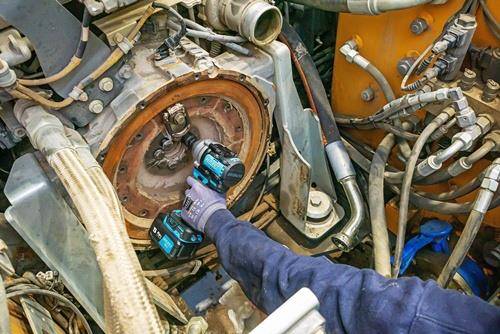 Eine Person, die ein Elektrowerkzeug verwendet, um eine Komponente des Fahrzeugmotors zu bearbeiten, umgeben von mechanischen Teilen und Werkzeugen.