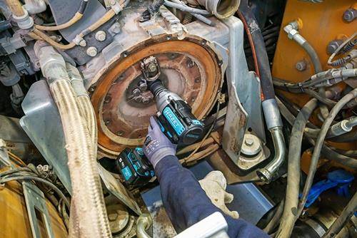 Eine Person mit Handschuhen verwendet einen Schlagschrauber, um einen Bolzen an großer Industriemaschine zu befestigen und dabei Reparatur- oder Wartungsarbeiten zu demonstrieren.