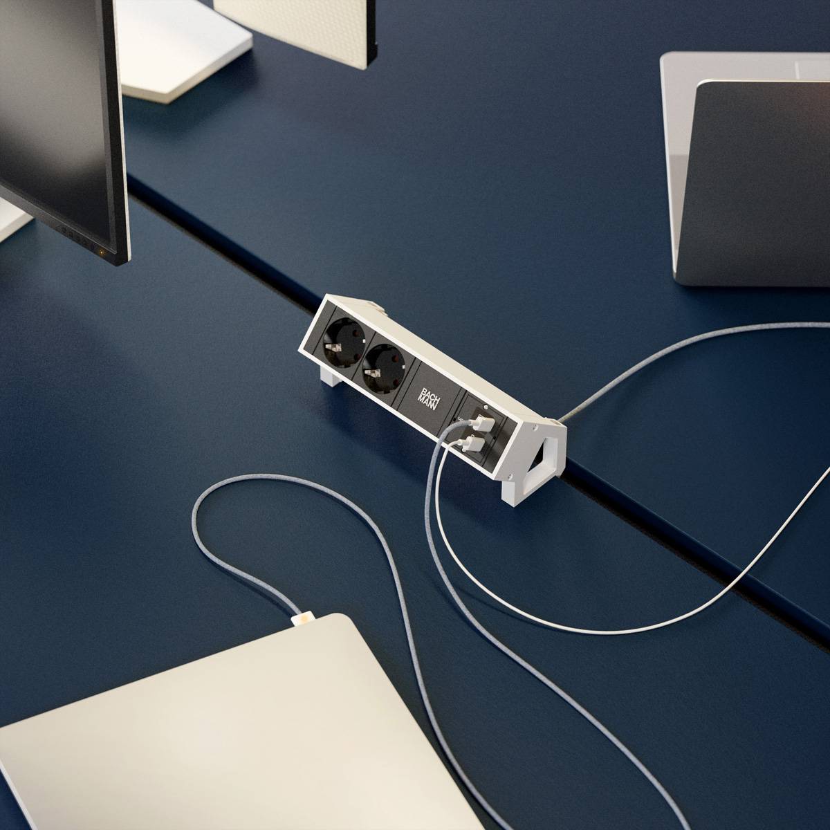 Ein moderner Büroschreibtisch verfügt über eine Steckdosenleiste mit drei Steckdosen und einem prominenten USB-Ladeanschluss, umgeben von Laptops und Bildschirmen.