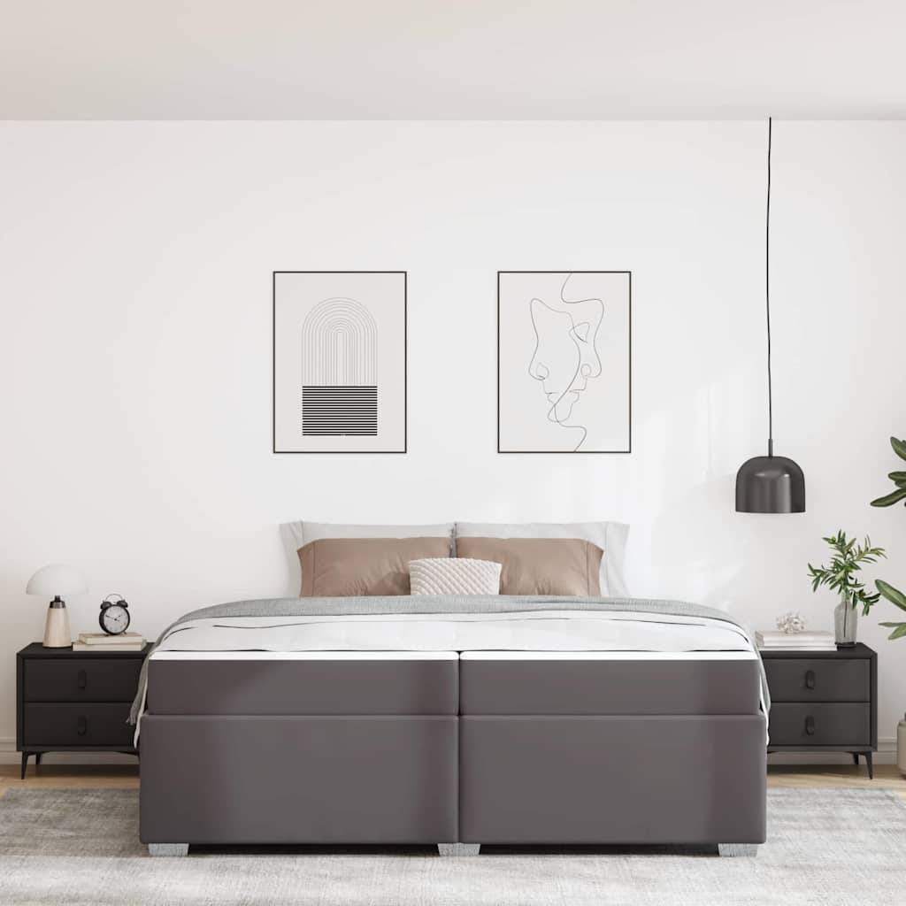 Modernes Schlafzimmer mit einem grau gepolsterten Bett, passenden Nachttischen, Wandkunst, hängender Pendelleuchte und einer Topfpflanze vor einer weißen Wand.