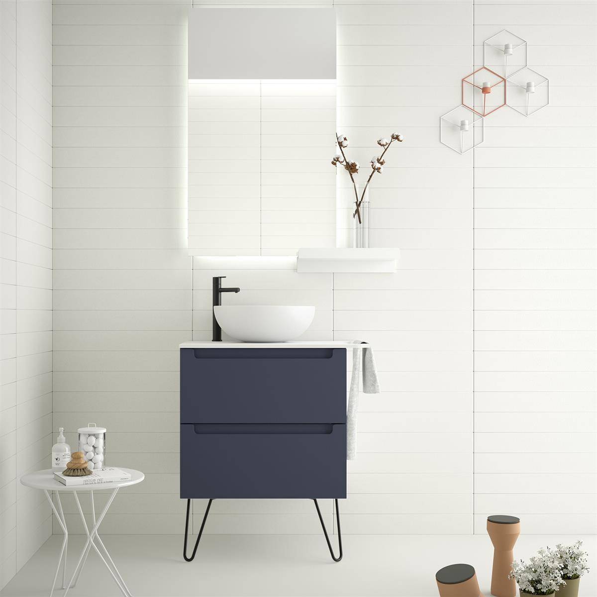 Minimales modernes Badezimmer mit marineblauer Waschtischanlage, weißem Aufsatzwaschbecken, beleuchtetem Spiegel, Wandregal mit Vase und kleinen Beistelltischen auf weißem Fliesenboden.