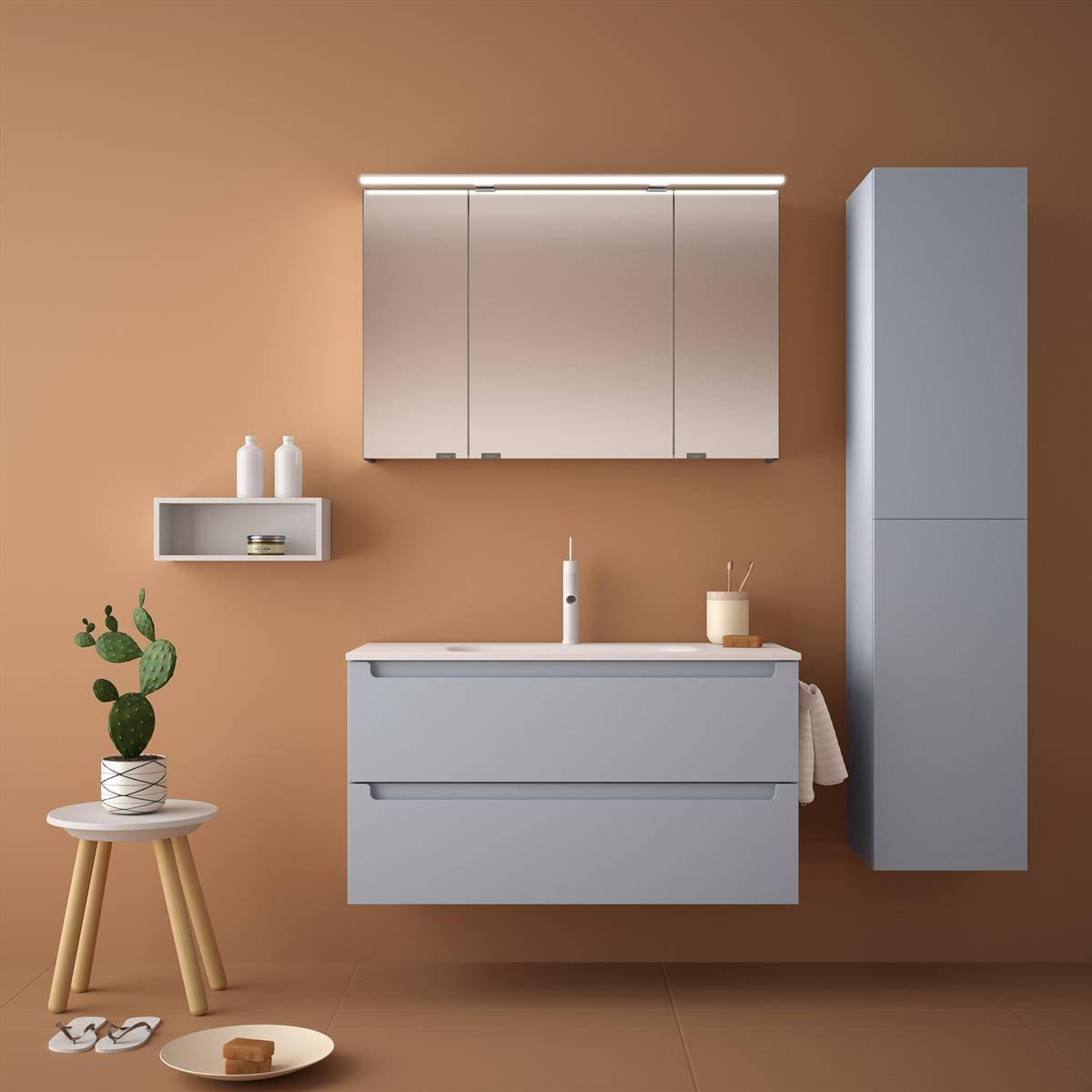 Minimalistische Badezimmerwaschbeckeneinrichtung mit grauem Schrank, verspiegeltem Arzneischrank, hohem Lagerschrank, Wandregal und kleiner Pflanze auf Hocker.