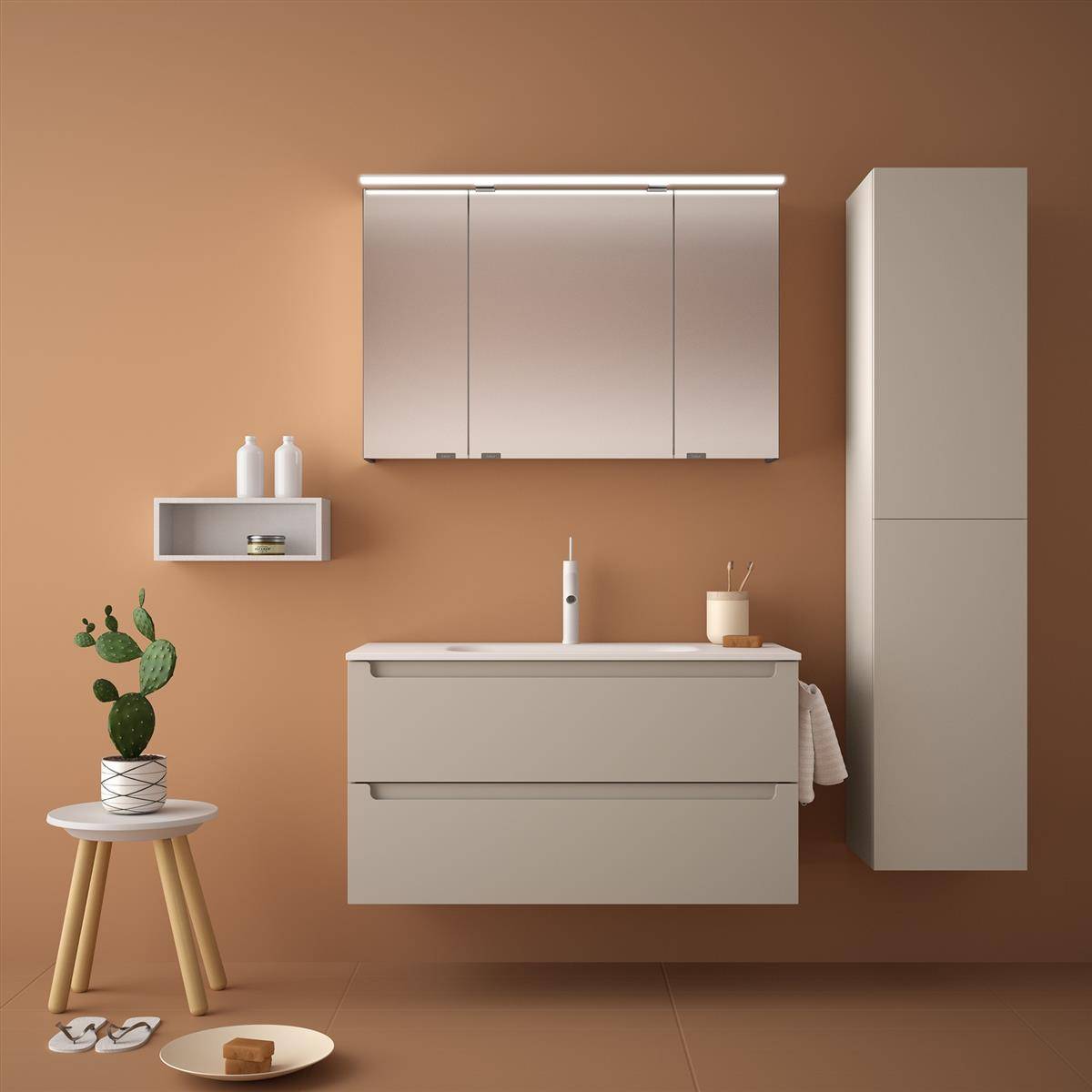Minimales Badezimmerinnere mit beigem Waschtisch, Wandschrank, hohem Lagerschrank, Regal, kleiner Pflanze und Accessoires vor einer warmen braunen Wand.
