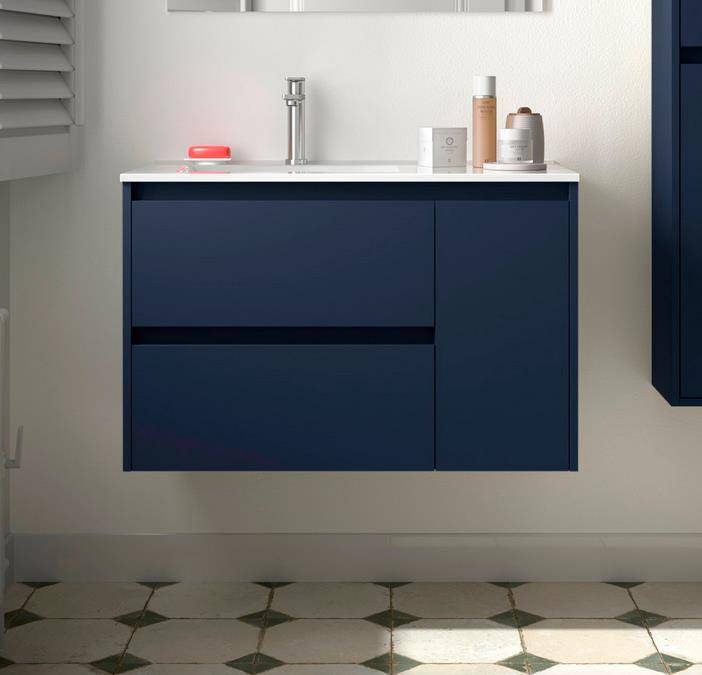 Wandmontiertes marineblaues Badezimmerwaschtisch mit weißer Spülenplatte und Chromarmatur, flankiert von Toilettenartikeln vor einer hellen Wand und gemustertem Fliesenboden.