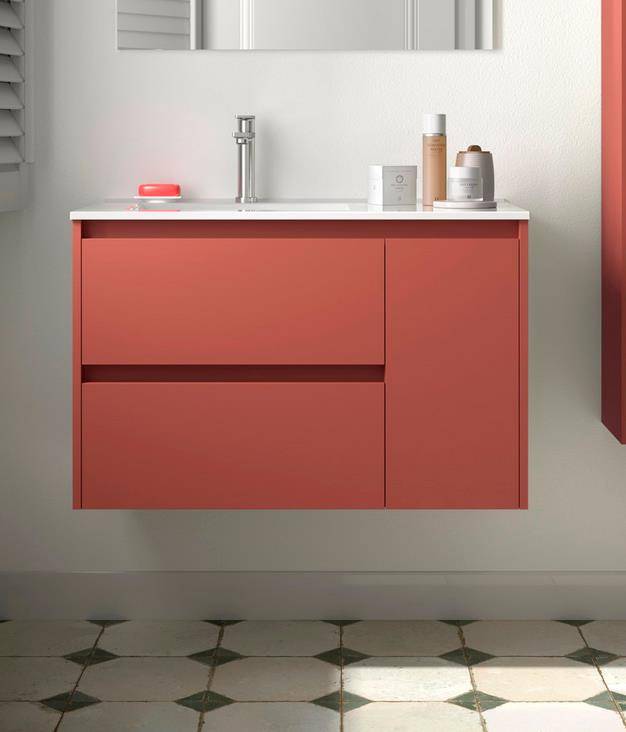 Modernes Badezimmerwaschtisch mit rotem schwebendem Schrank, weißer Arbeitsplatte, Waschbecken, Armatur, Spiegel und Toilettenartikeln über gemustertem Fliesenboden.