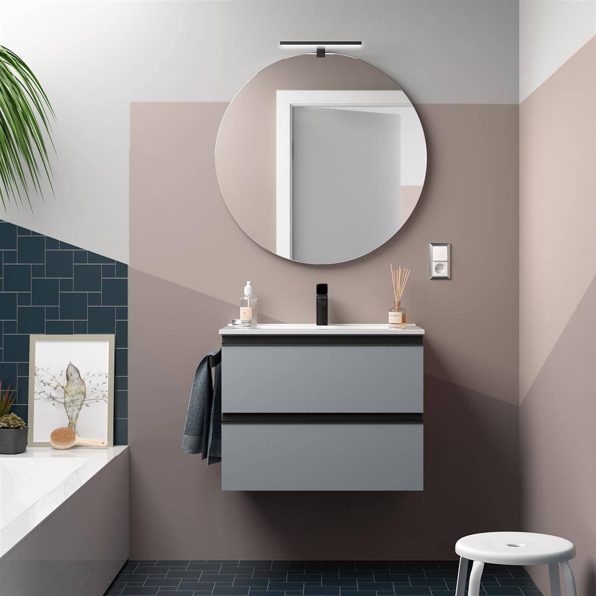 Modernes Badezimmer mit grauem schwebendem Waschtisch, rundem Spiegel, Wandleuchte und weißem Hocker neben einem gekachelten Badewannenbereich.