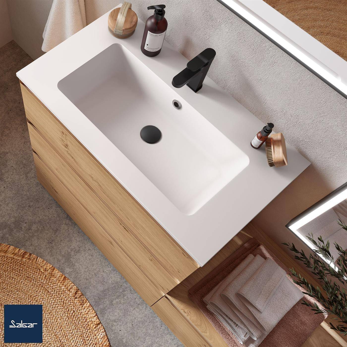 Modernes Badezimmermöbel mit weißem Waschbecken und schwarzem Wasserhahn, Unterschrank aus hellem Holz, Seifenspender, Bürste und gefaltete Handtücher.