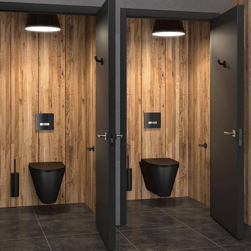 Zwei benachbarte moderne Toilettenkabinen mit schwarzen Toiletten, Holzverkleidung an den Wänden, dunklen Türen und Deckenleuchten auf einem dunklen Fliesenboden.