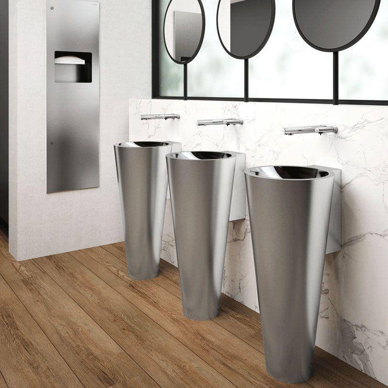 Modernes Badezimmer mit drei Edelstahl-Säulenbecken, runden Spiegeln und einem wandmontierten Papierhandtuchspender auf einem Holzboden.