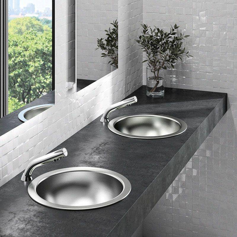 Modernes Badezimmer-Waschtisch mit zwei runden Unterbau-Waschbecken, Chromarmaturen, dunkler Arbeitsplatte, Wandspiegel und kleinen Topfpflanzen neben einem Fenster.