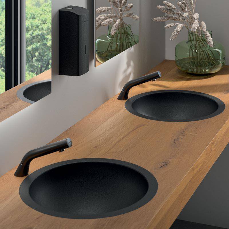 Modernes Badezimmerwaschtisch mit zwei schwarzen Aufsatzwaschbecken, mattschwarzen Armaturen und einer Holzarbeitsplatte neben einem Fenster und einer dekorativen Vase mit Trockenblumen.