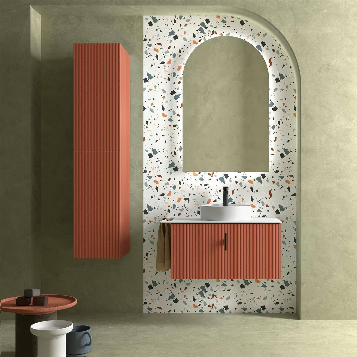 Modernes Badezimmerwaschtisch mit einem terrazzo-gerahmten Spiegelbogen, korallengerieftem Unterschrank, Waschbecken, Handtuch und passendem hohem Wandschrank an einer salbeigrünen Wand.