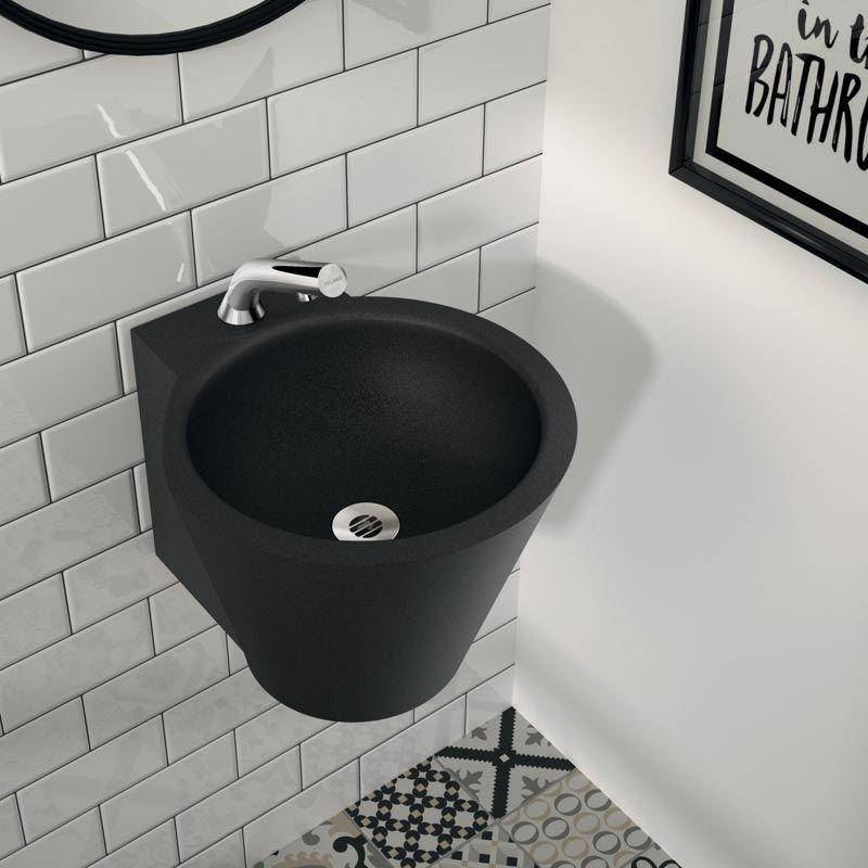 Ein schwarzes an der Wand montiertes Waschbecken mit einem Wasserhahn befindet sich in einer gekachelten Badezimmerecke über gemusterten Bodenfliesen.