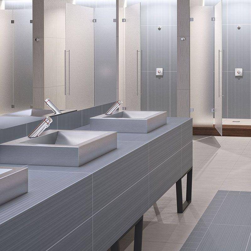 Modernes öffentliches Badezimmer mit einer Reihe von Waschbecken, Spiegeln und privaten Duschkabinen in einem sauberen, grau gefliesten Innenraum.