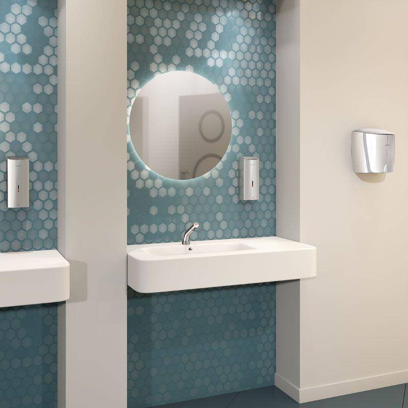 Modernes Waschbecken mit rundem Spiegel, weißem Waschbecken, Wand mit türkisfarbenen Sechskant-Fliesen als Akzentwand und an der Wand montiertem Spender; angrenzende schlichte Wand mit einem weiteren Spender.