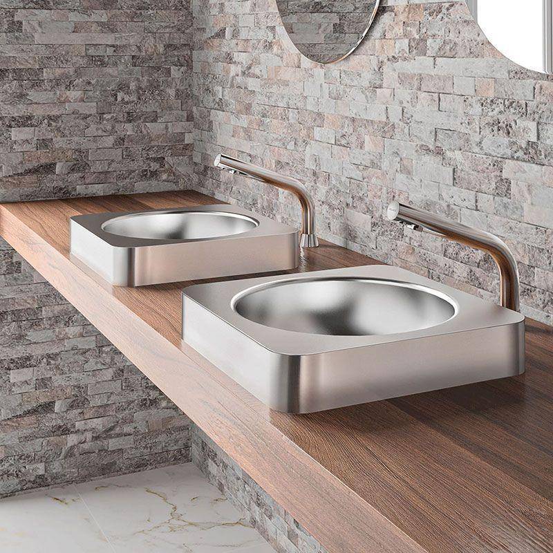 Zwei moderne Waschbecken aus gebürstetem Metall mit wandmontierten Armaturen auf einer Holzarbeitsplatte vor einer Steinfliesenwand.