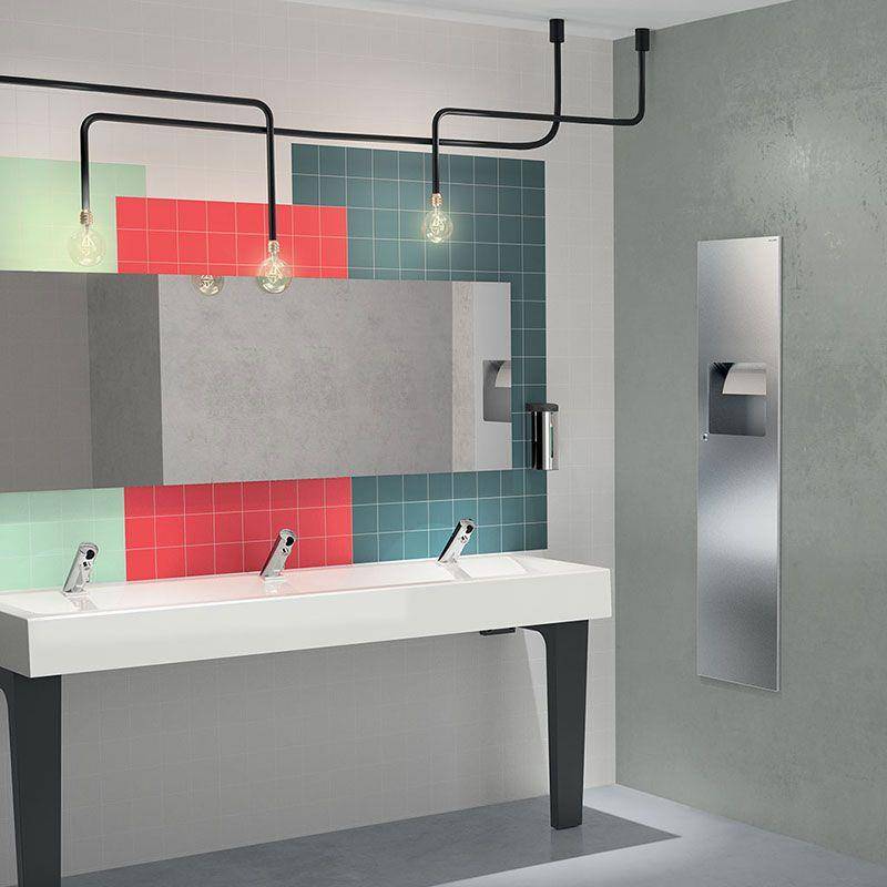 Modernes Badezimmer-Waschbecken mit langem weißem Becken, farbenfrohem Fliesenspritzschutz, großem Spiegel, hängenden Glühbirnen und an der Wand montiertem Toilettenpapierhalter.