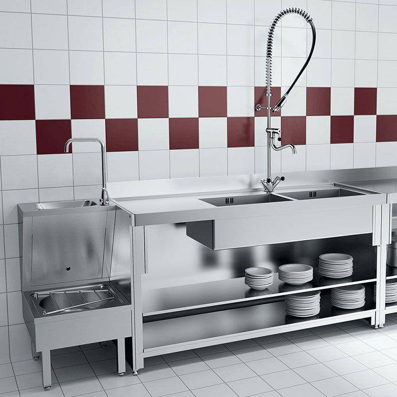 Kommerzielle Edelstahlküchenspüleneinheit mit zwei Wasserhähnen, tiefem Becken, Handwaschbecken und offenen Regalen, auf denen Teller gestapelt sind, an einer gekachelten Wand.