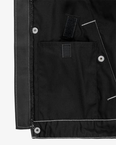 Das Bild zeigt das Innere einer schwarzen Jacke mit einer Pattentasche und einem Klettverschluss, hervorgehoben durch weiße Nähte entlang der Kanten.